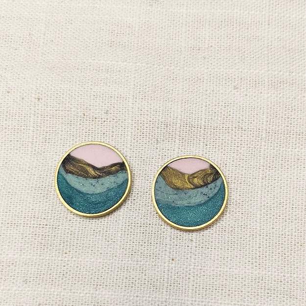 A circular earring set that includes layers of pink, gold, mint green, and teal clay with shimmer throughout.